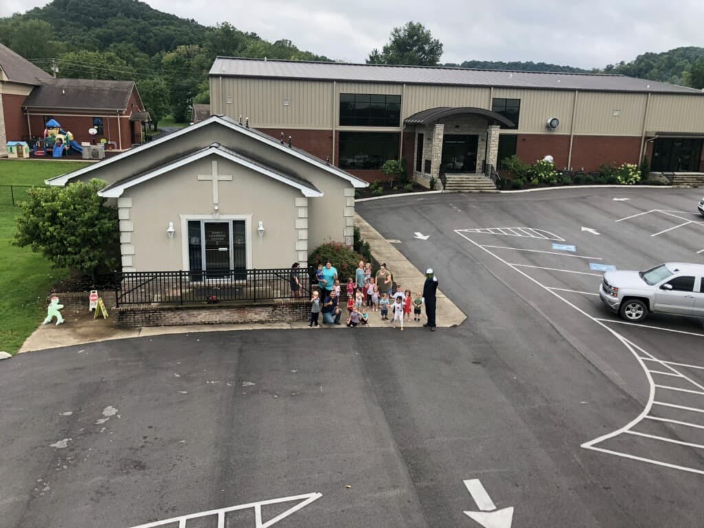 Group of people and children standing outside a small building with a cross