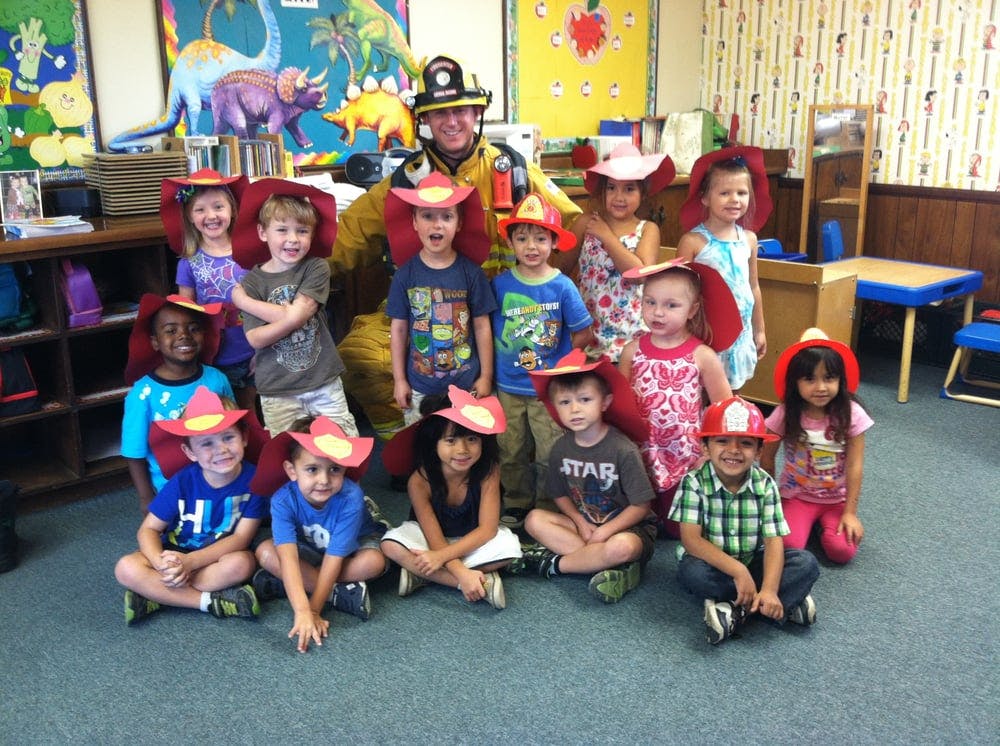 Firefighter posing with a group of children wearing red hats in a classroom
