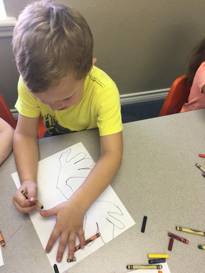Child tracing their hand on paper with a crayon