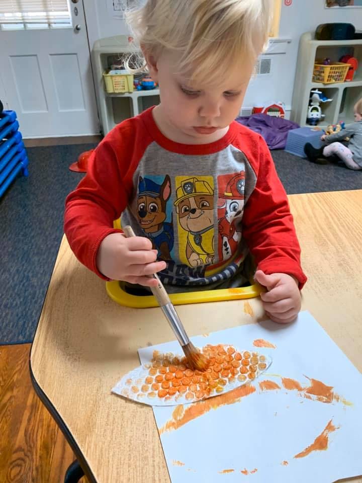 Child painting with a brush on paper with orange dots