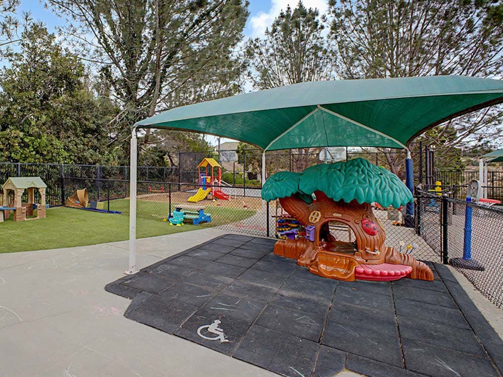 Playground area with a tree-shaped playhouse under a green shade