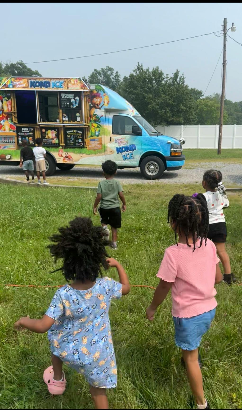 Group of children running across grass toward a Kona Ice truck