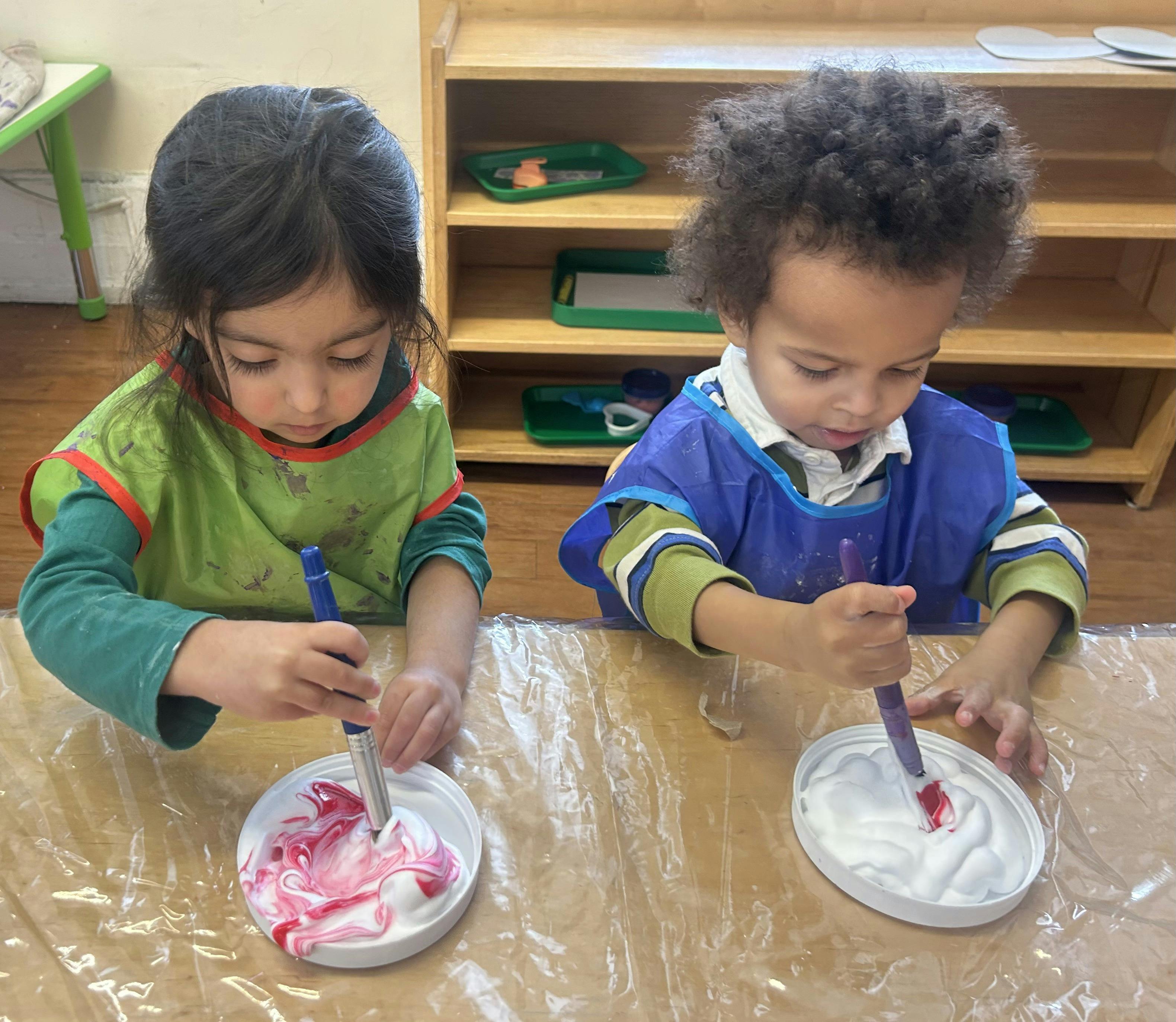 Two children in smocks mixing paint in shaving cream
