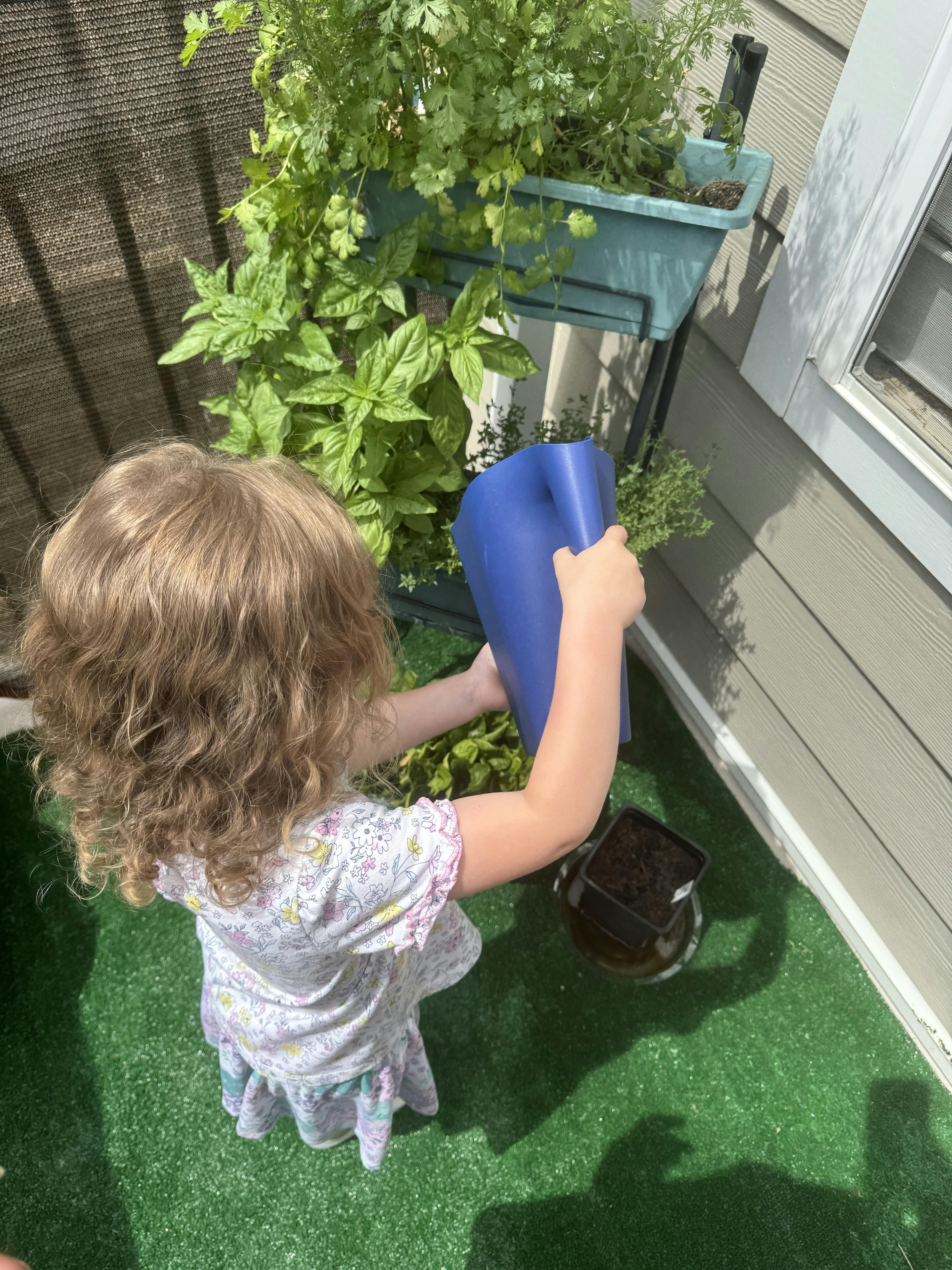 Child watering potted plants on a balcony