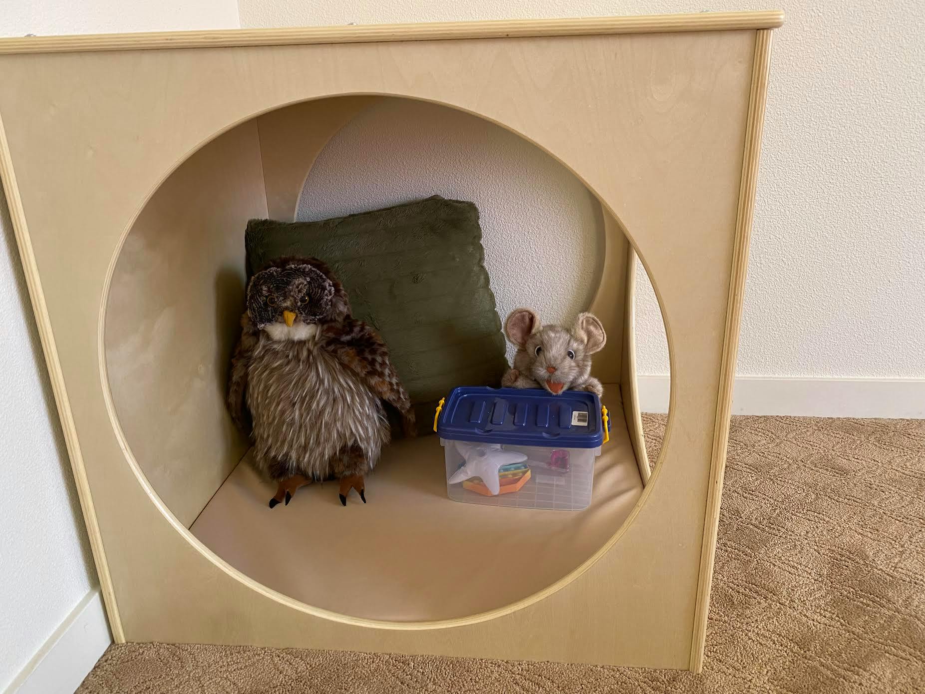 Stuffed owl and mouse in a wooden cubby with a green pillow