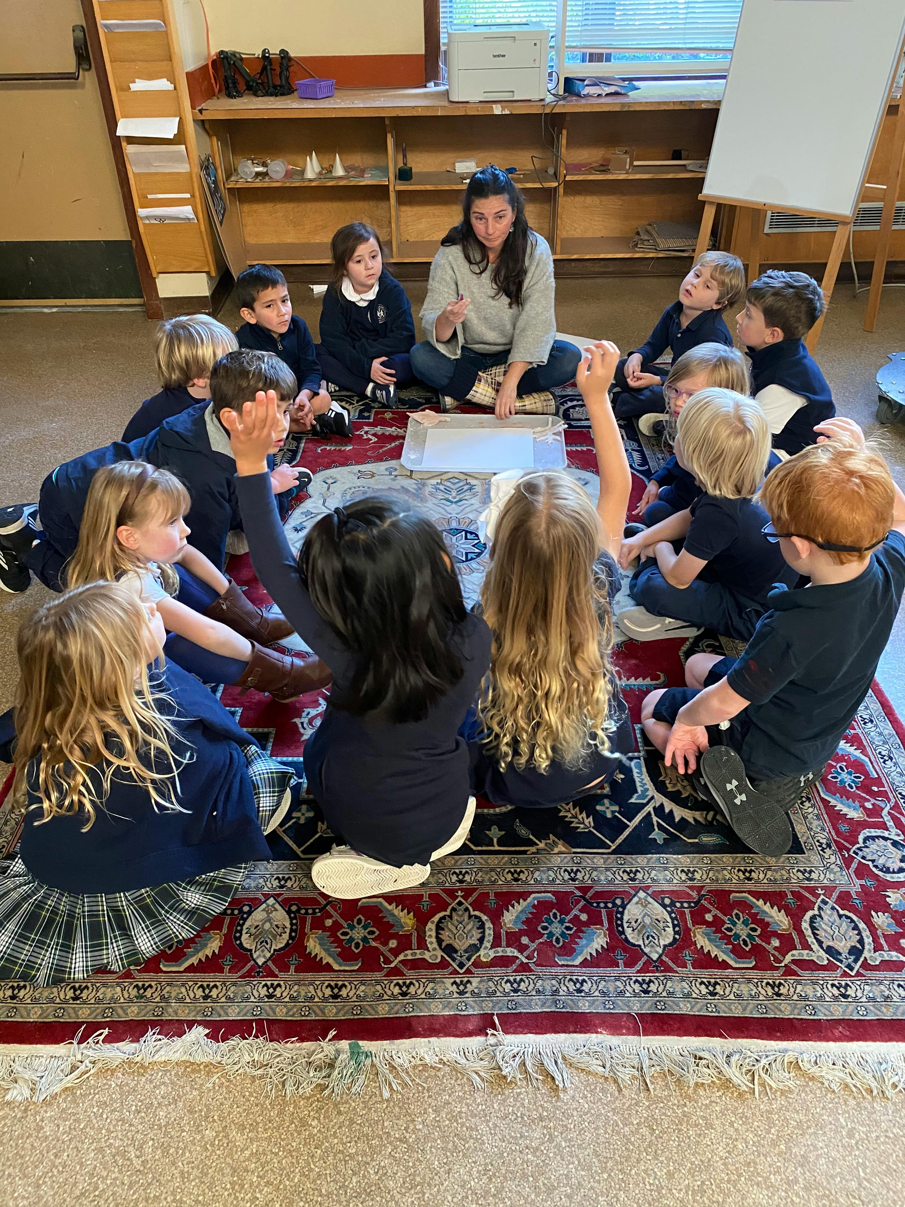 Adult and children sitting in a circle on a rug in a classroom