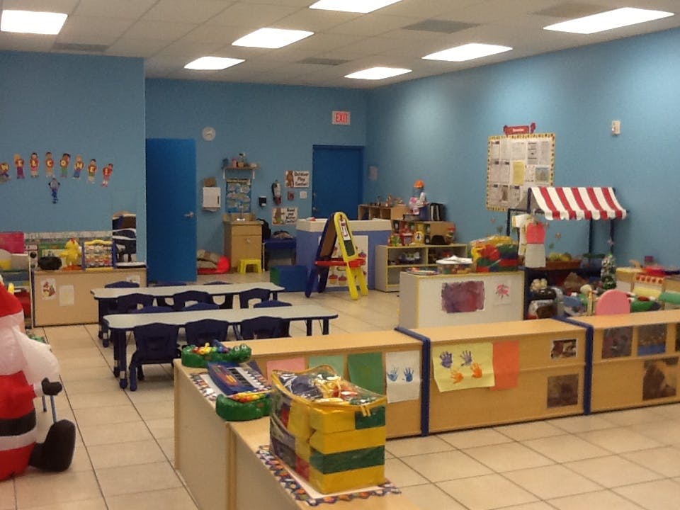 Classroom with small tables and chairs, play kitchen, and toy market stall