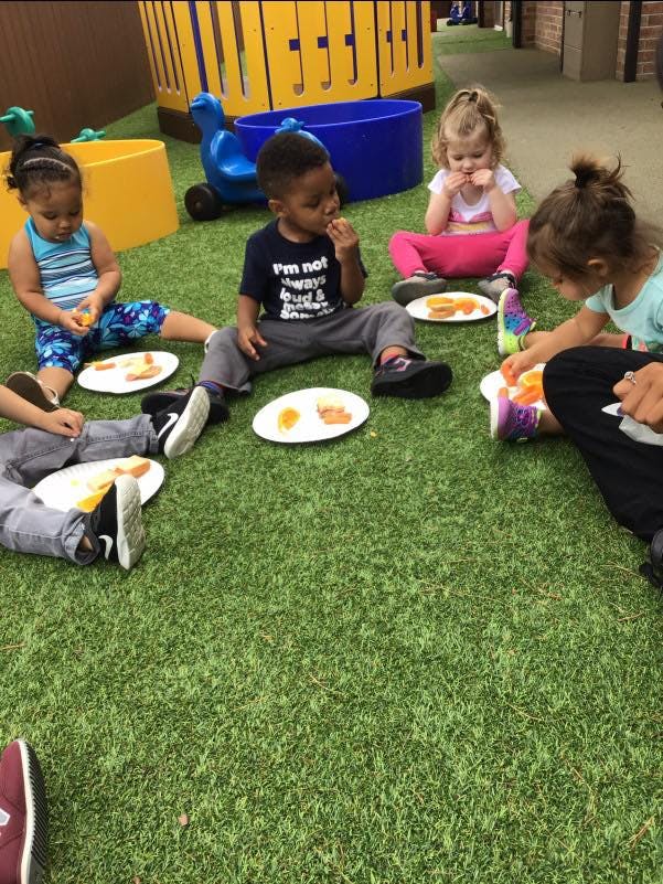 Children sitting on grass eating snacks from plates