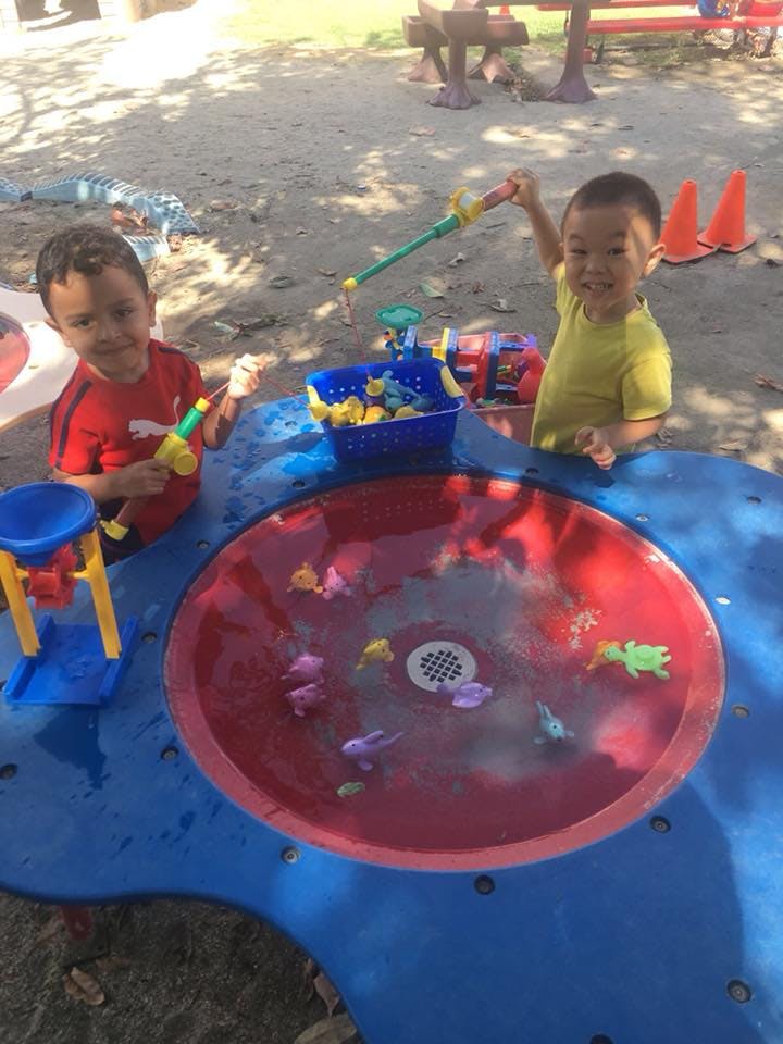 Two children playing with fishing toys at a water table
