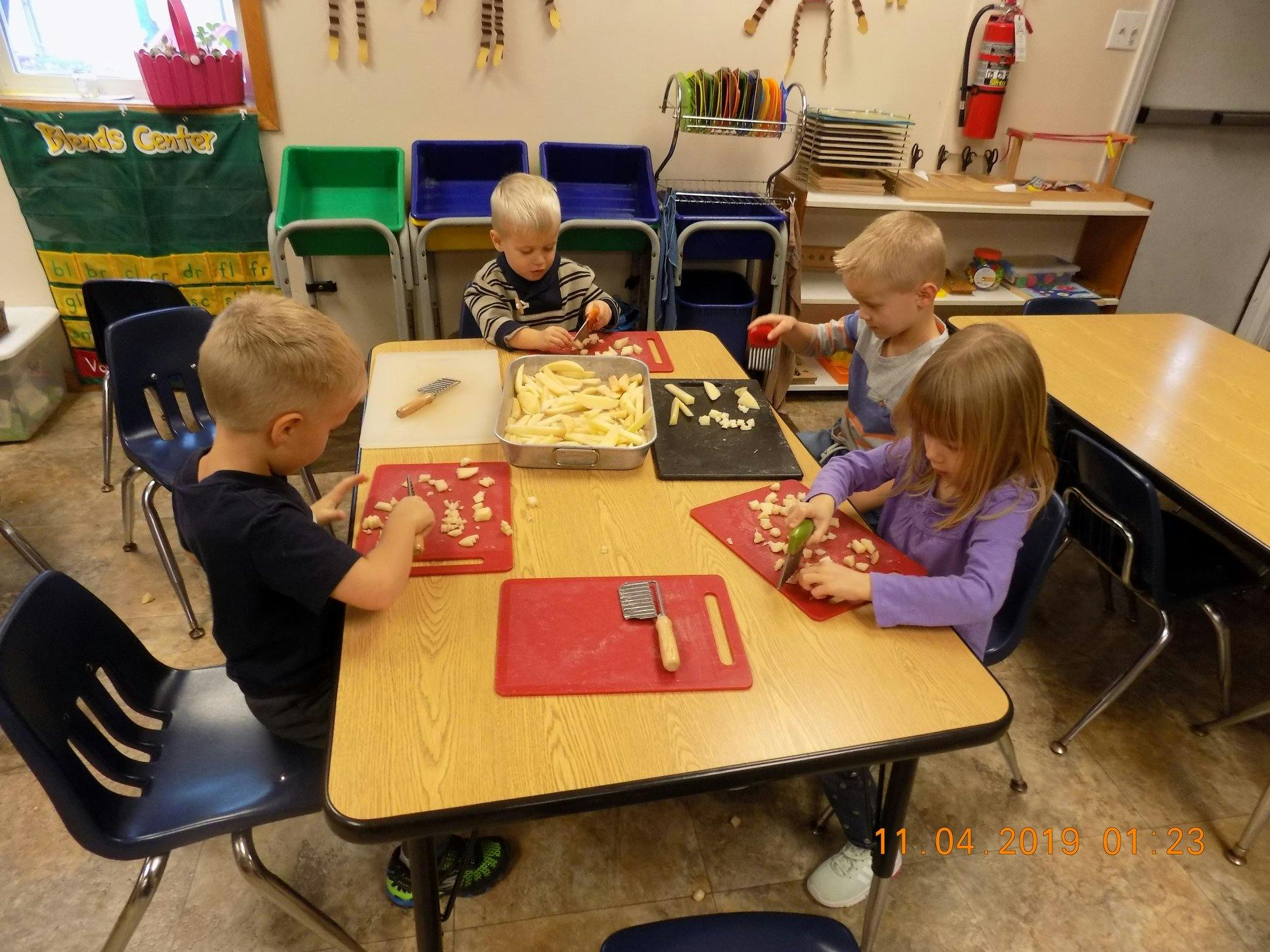 Four children at a table cutting food on red cutting boards