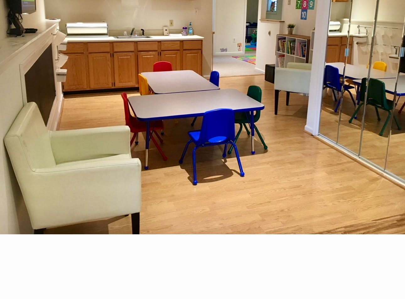 Room with small tables and colorful chairs, a white armchair, and wooden cabinets