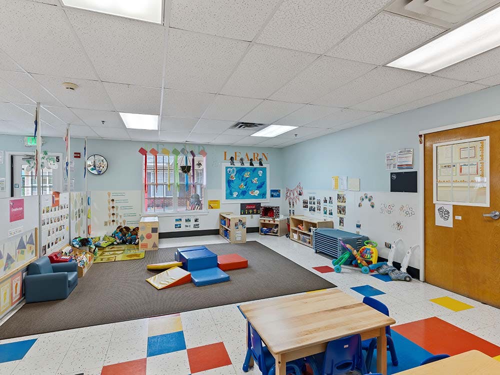 Classroom with child-sized furniture, colorful flooring, and play equipment