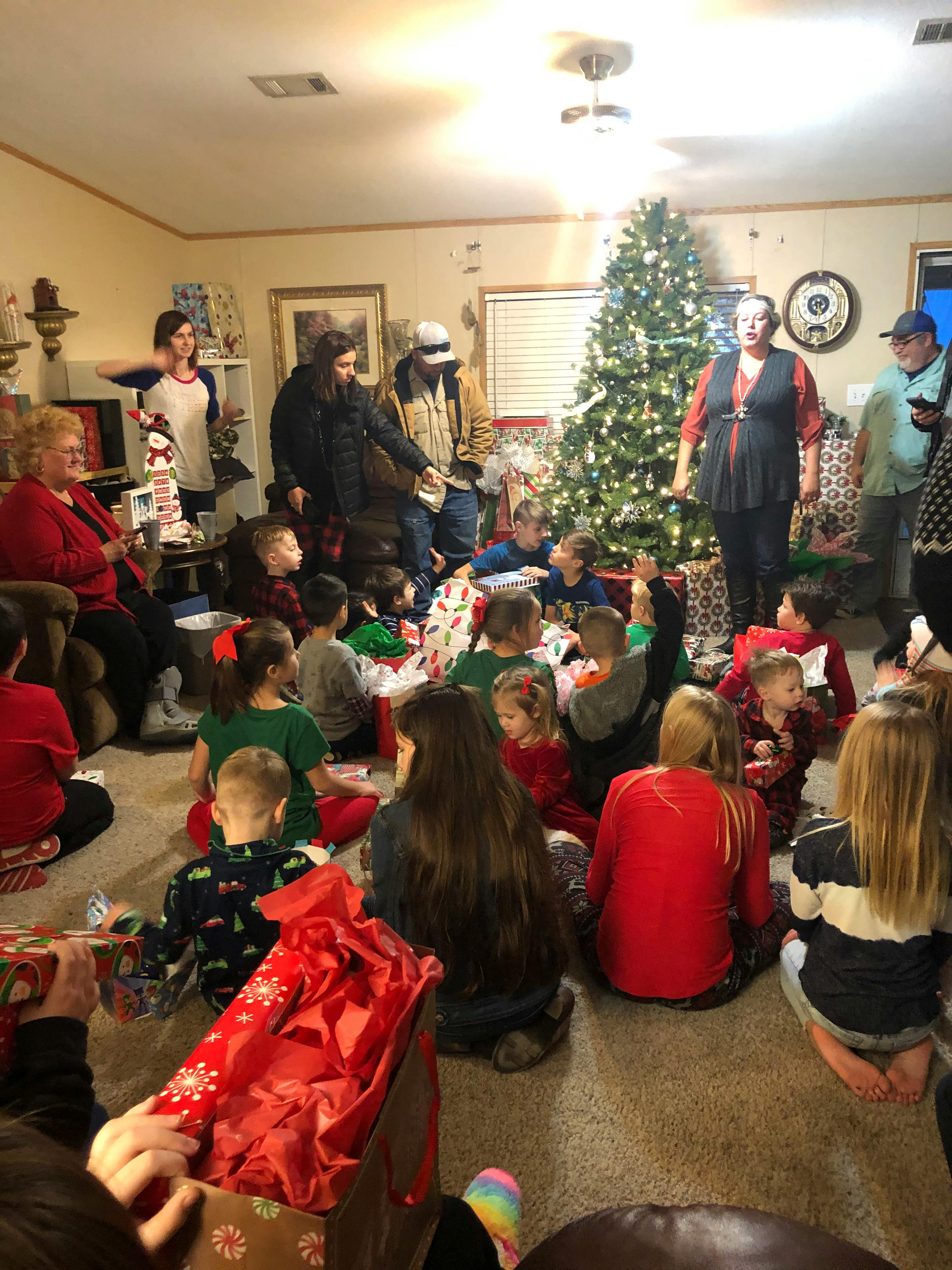 People and children gathered around a Christmas tree with gifts