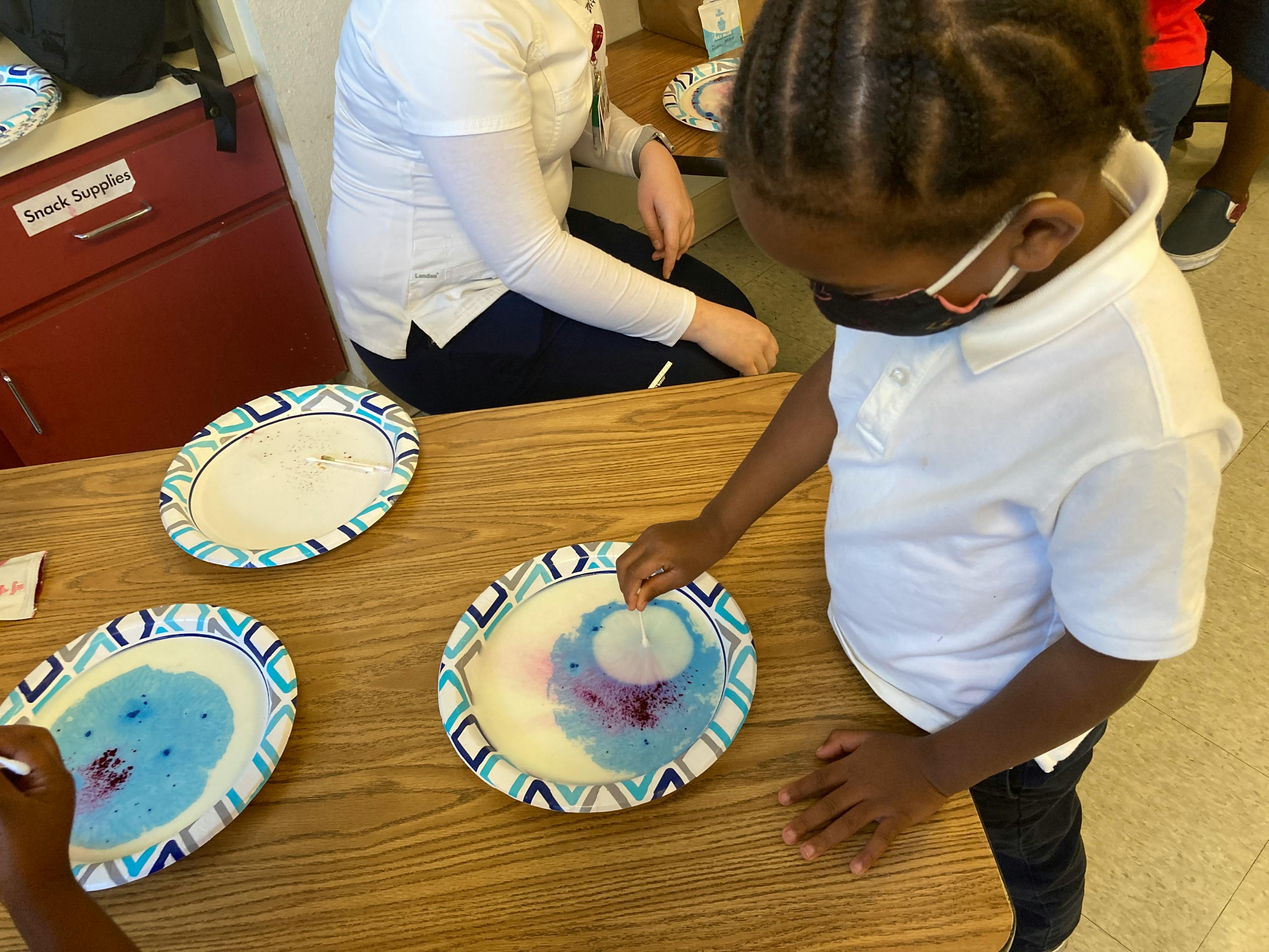 Child in a mask doing a science experiment with colored liquid on a plate