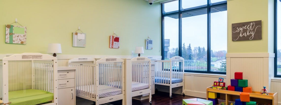 Multiple white cribs in a room with large windows and a sign that says "sweet baby"