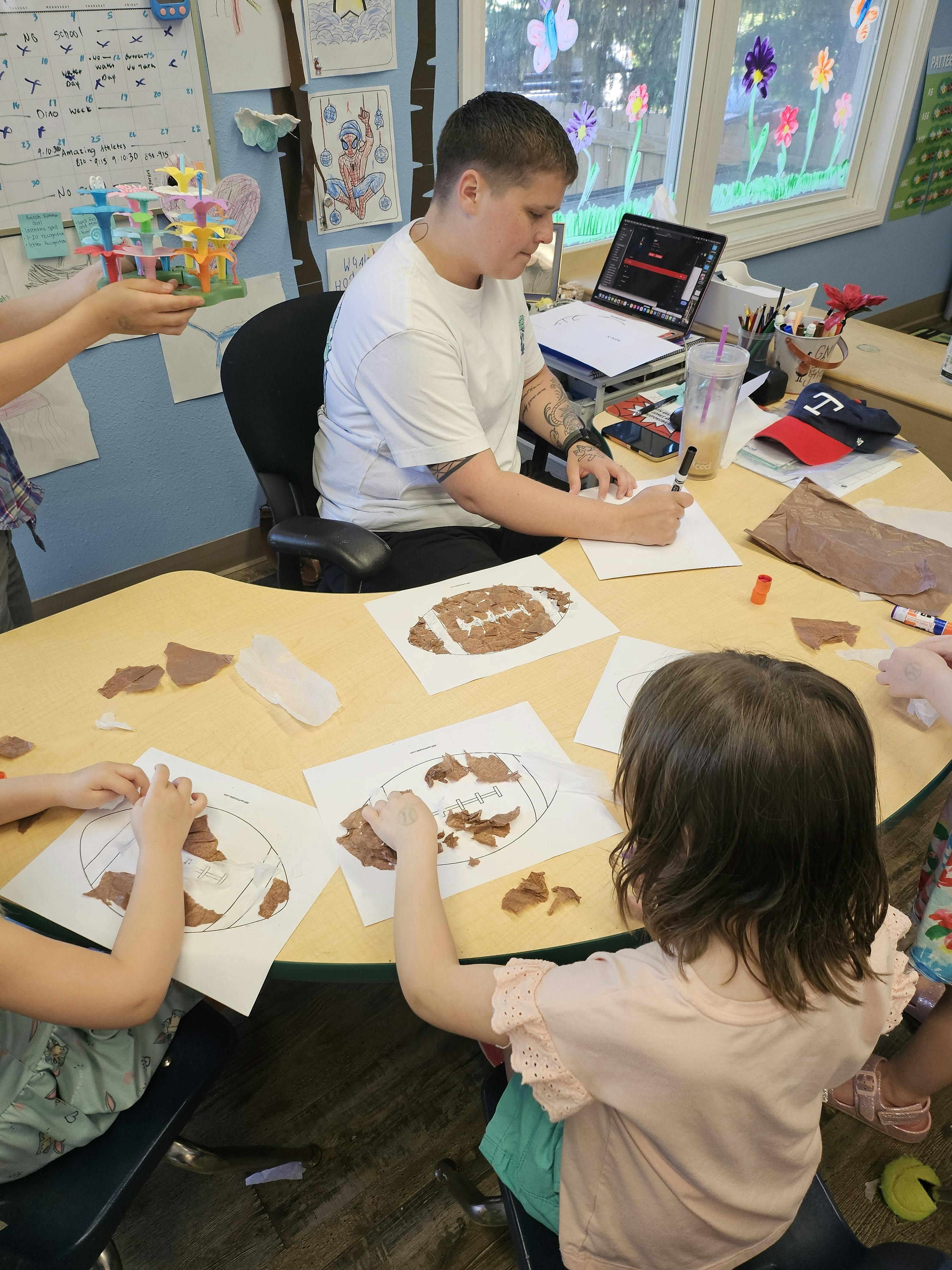 Person at desk with laptop, children making crafts at crafts at a table