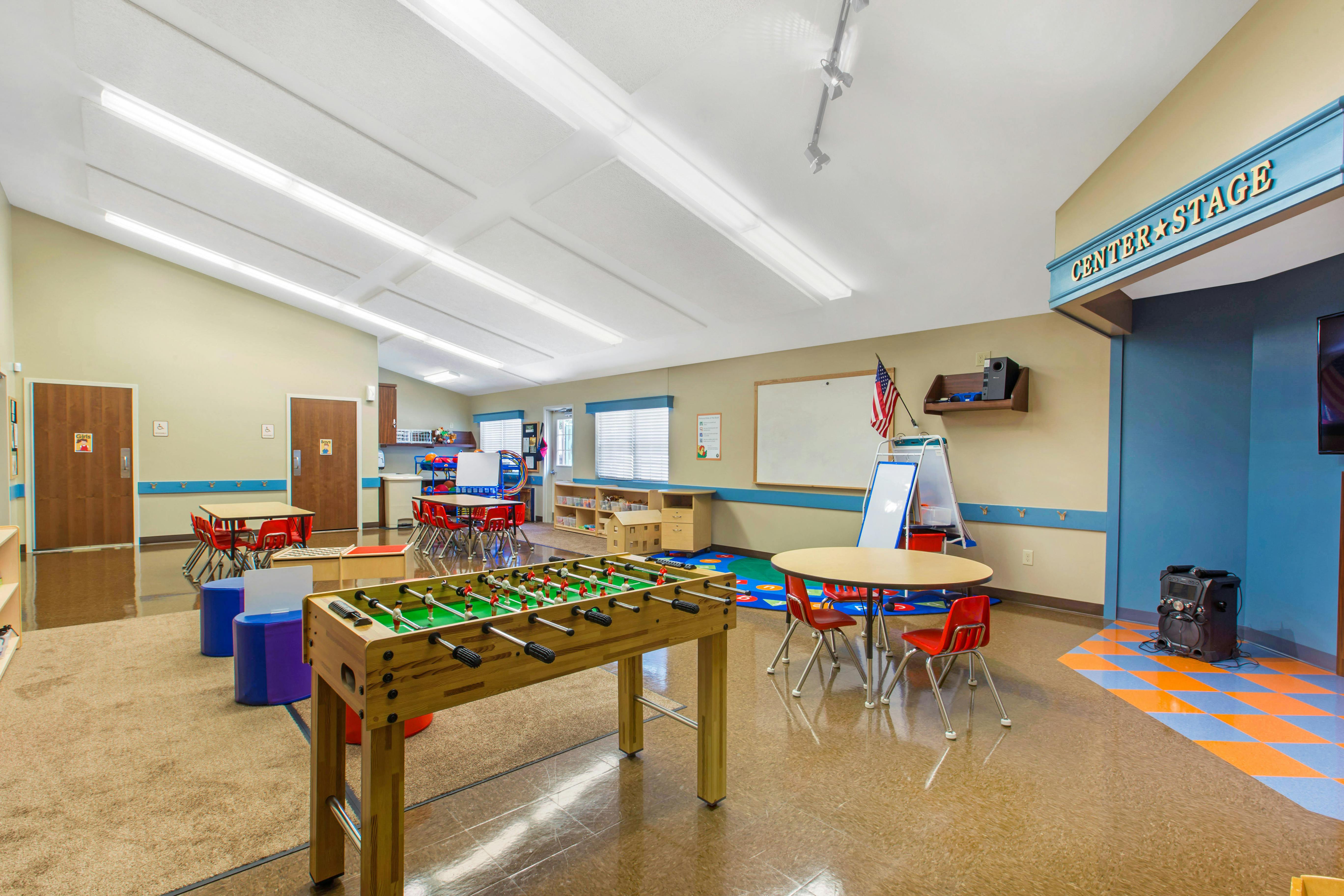 Classroom with child-sized tables and chairs, a foosball table, and a sign that reads "Center Stage"