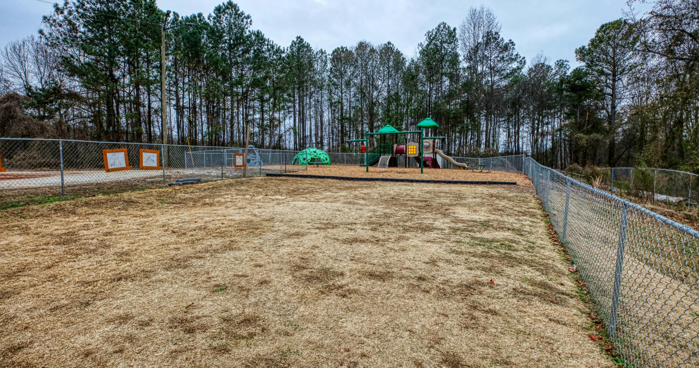 Empty playground with colorful equipment and a climbing dome behind a chain-link fence