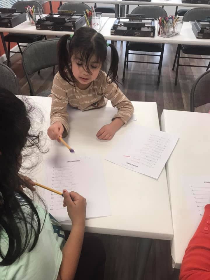 Two children sitting at a table with papers and pencils