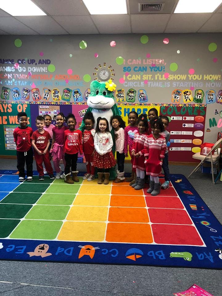 Children and a mascot standing on a colorful rug in a classroom