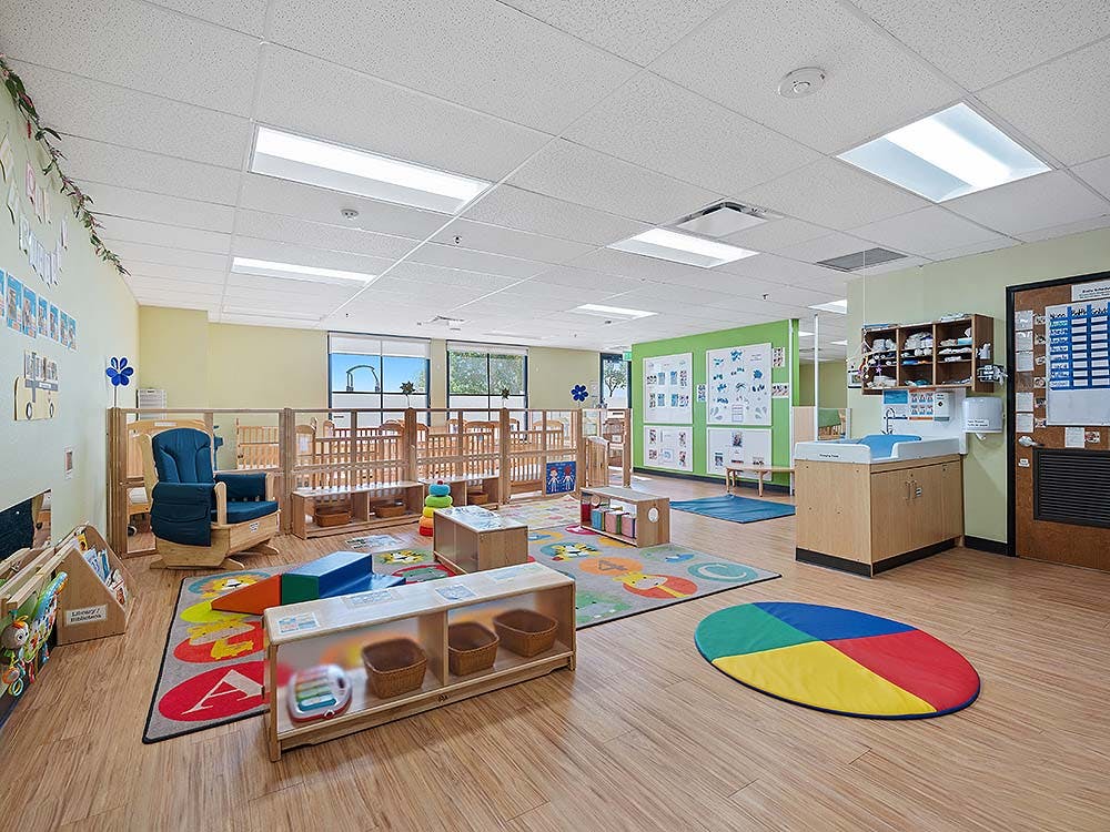 An empty daycare room with cribs, playmats, a rocking chair, and a changing table