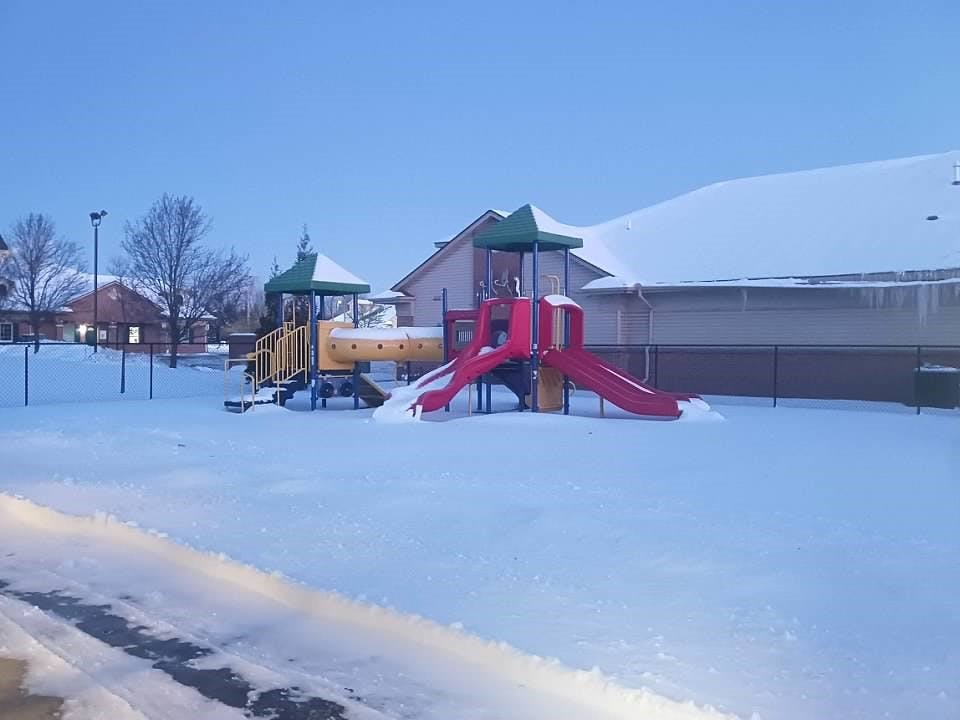 Snow-covered playground with red slides and yellow climbing structure