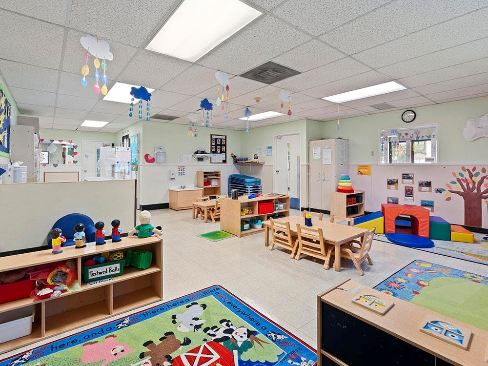Empty colorful preschool classroom with small tables, chairs, and play equipment