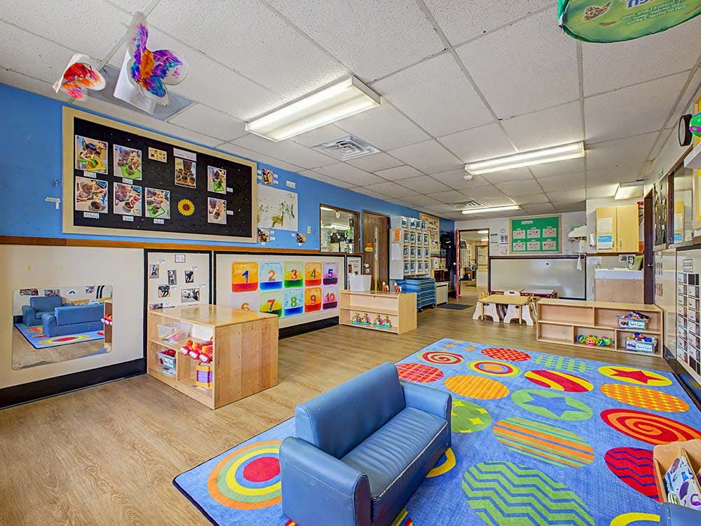 Classroom with colorful rug, blue walls, a small sofa, and children's art displays