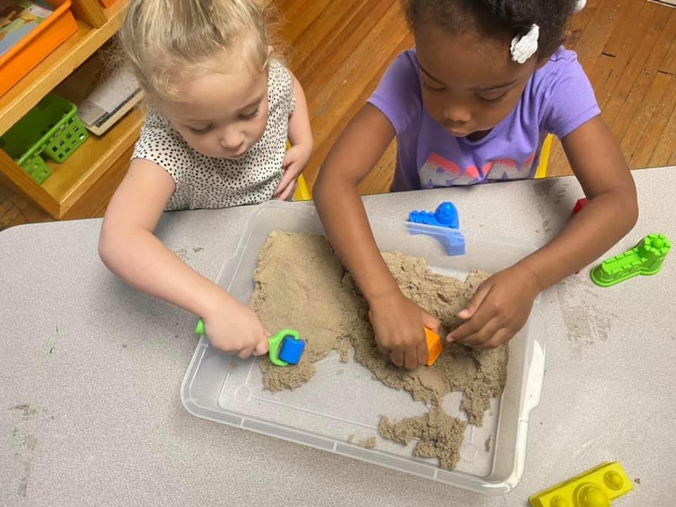 Two children playing with kinetic sand and toys at a table
