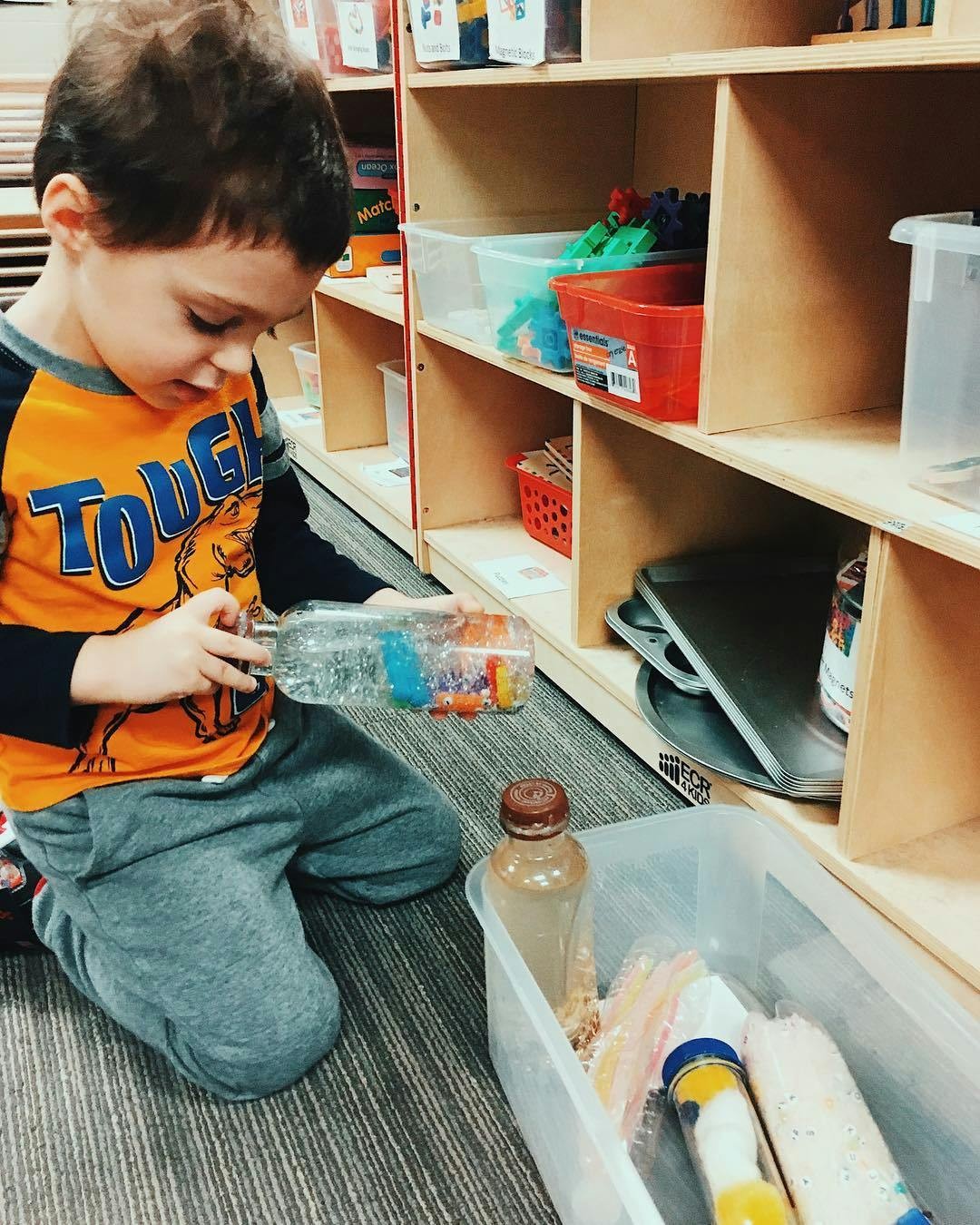 Child kneeling and holding a clear bottle with colorful items inside
