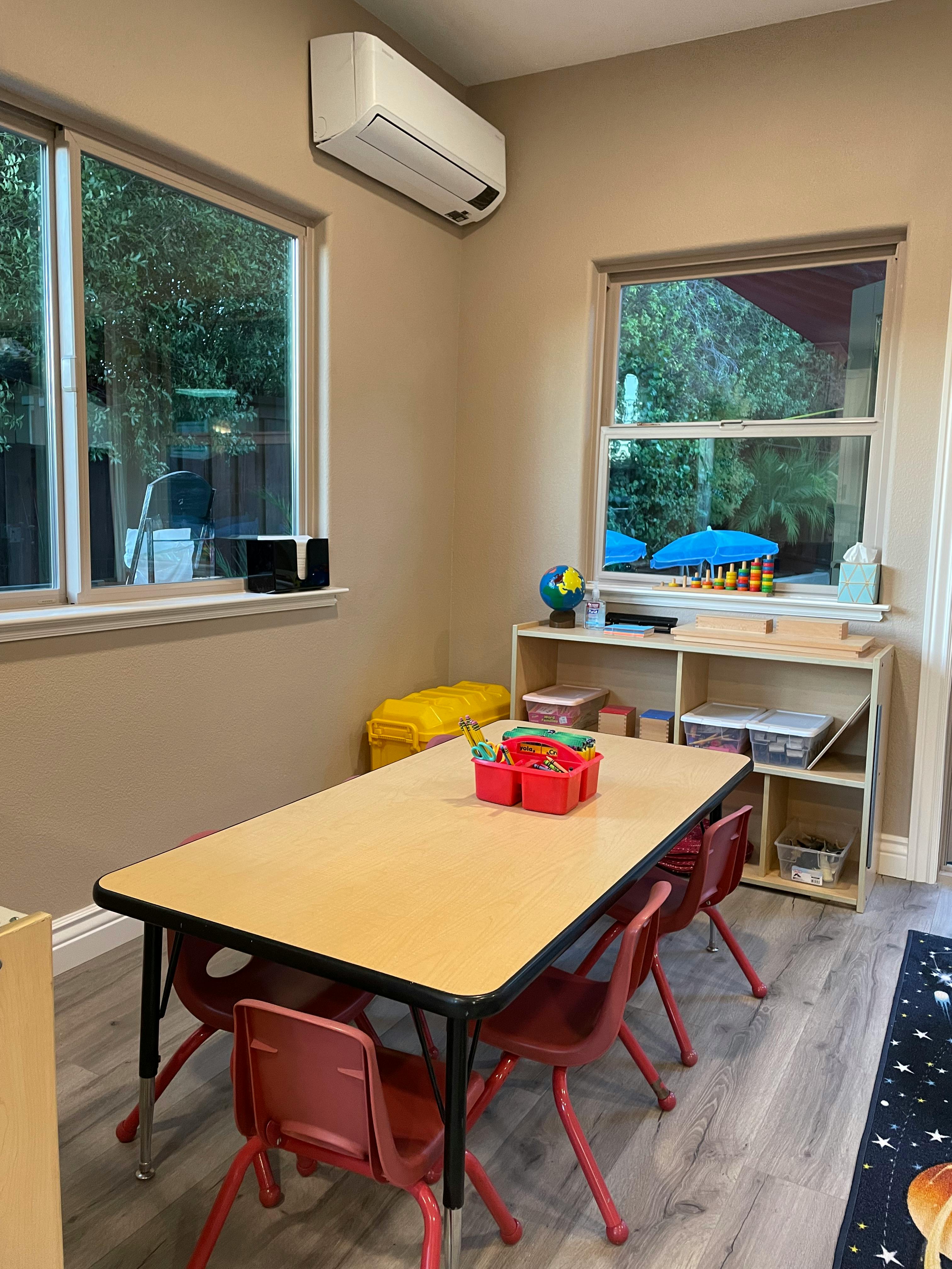 Classroom with a table and chairs, windows, and shelves
