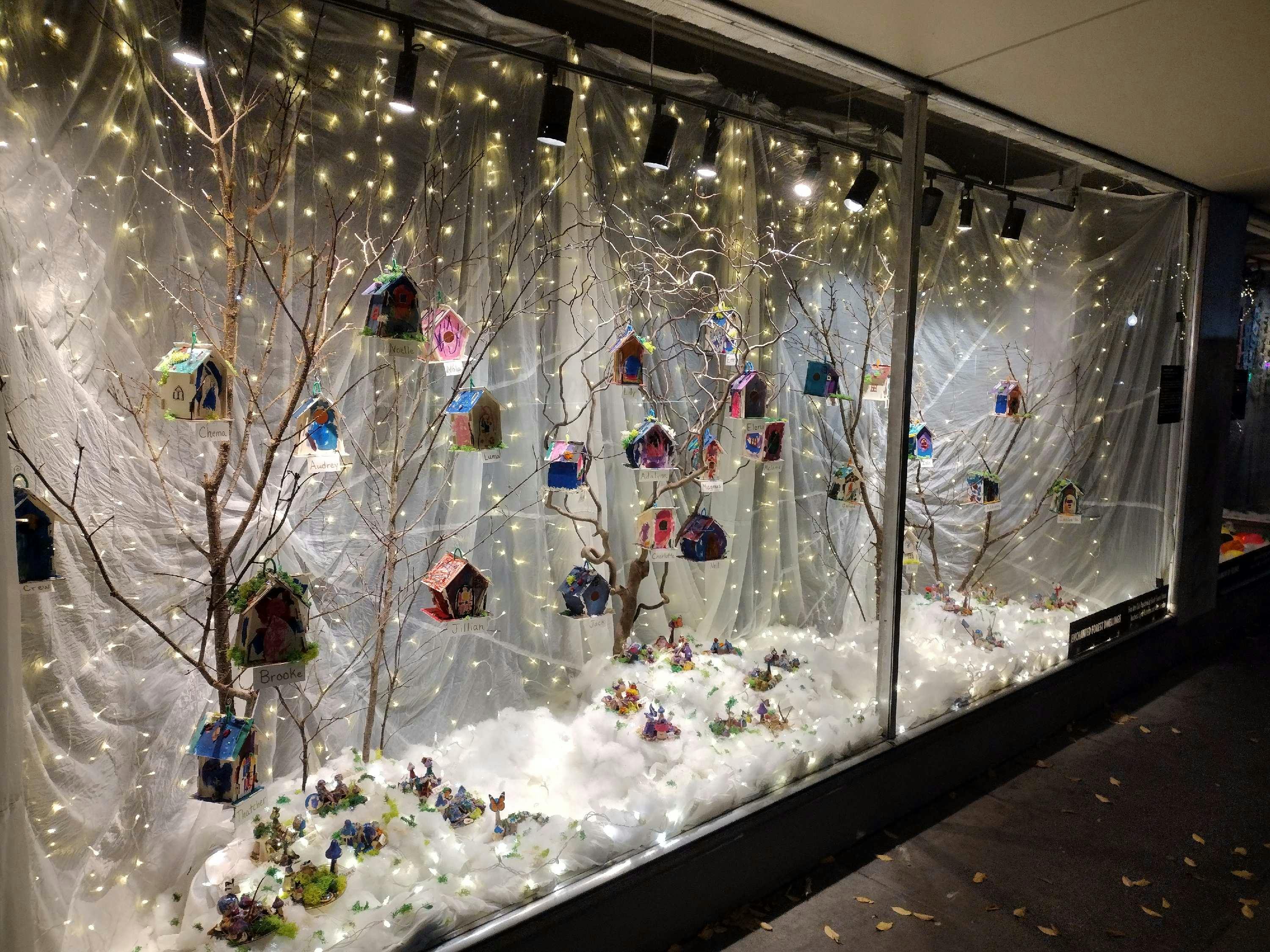 Store window display with bare trees, birdhouses, and string lights