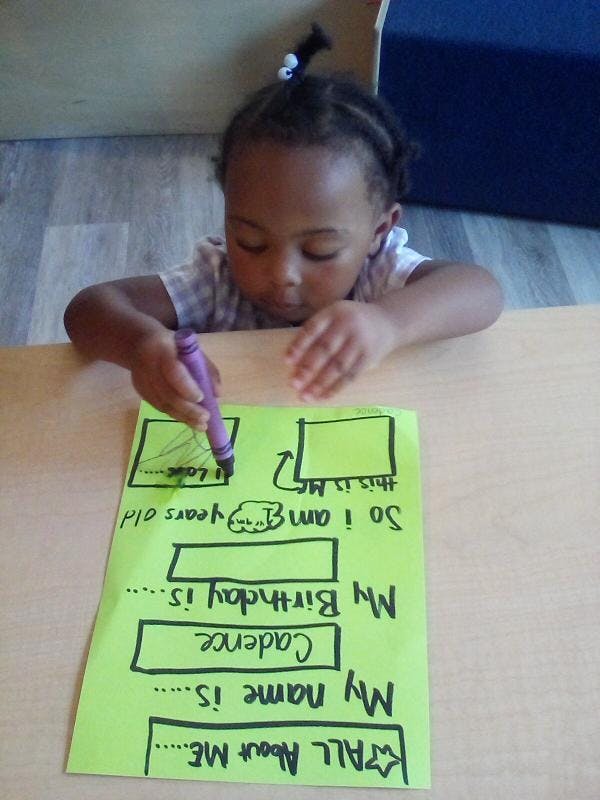 Child writing on a green paper with a purple crayon