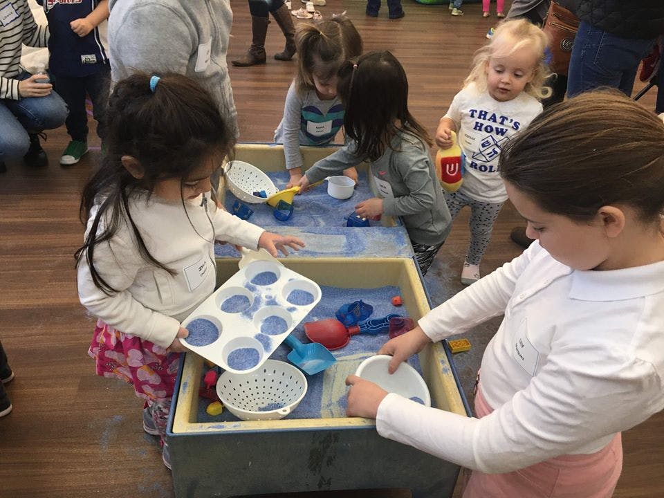 Children playing at a sensory table with sand and toys