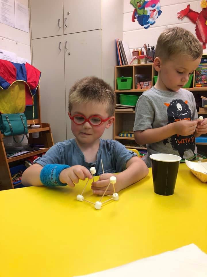 Two children building structures with marshmallows and toothpicks at a table