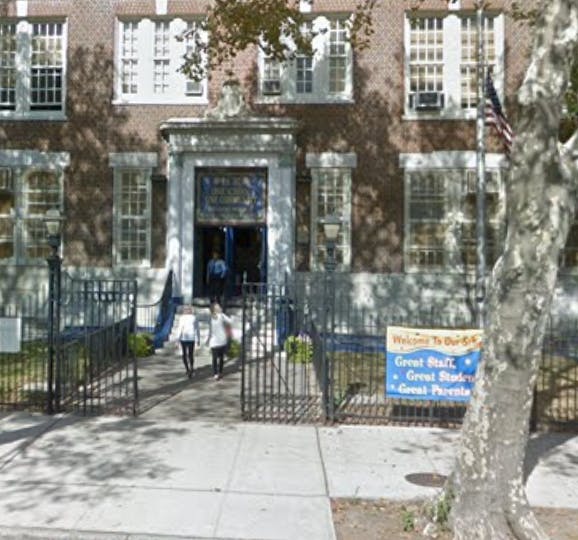 Two children walking through a gate towards a building entrance