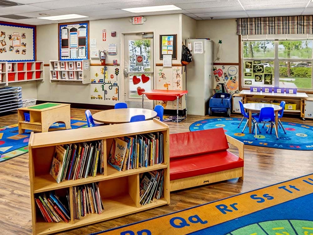 Empty classroom with small tables, chairs, and a bookshelf filled with books