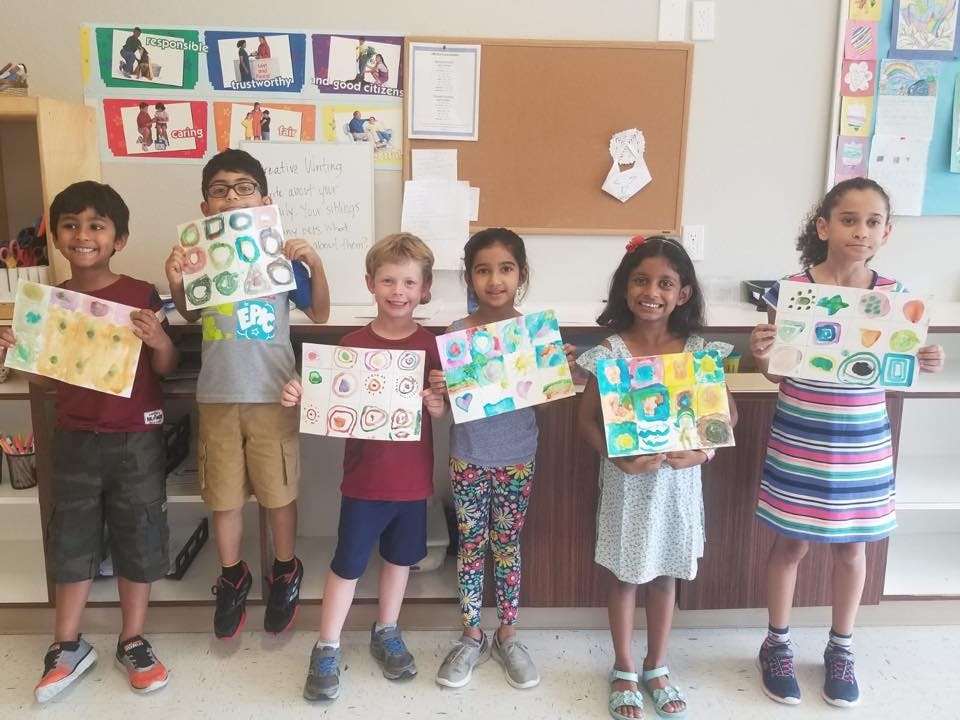 Six children holding up their artwork in a classroom