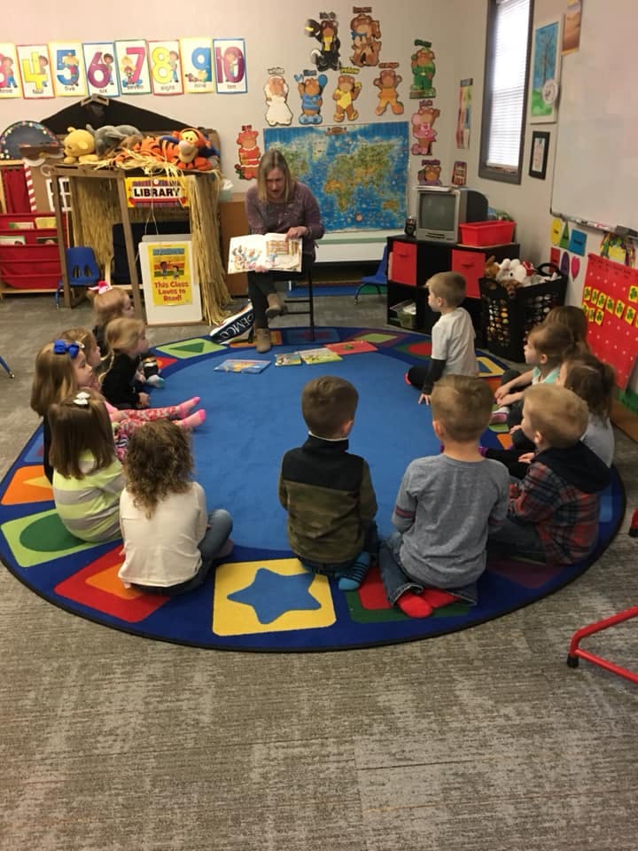 Adult reading a book to a group of children in a classroom