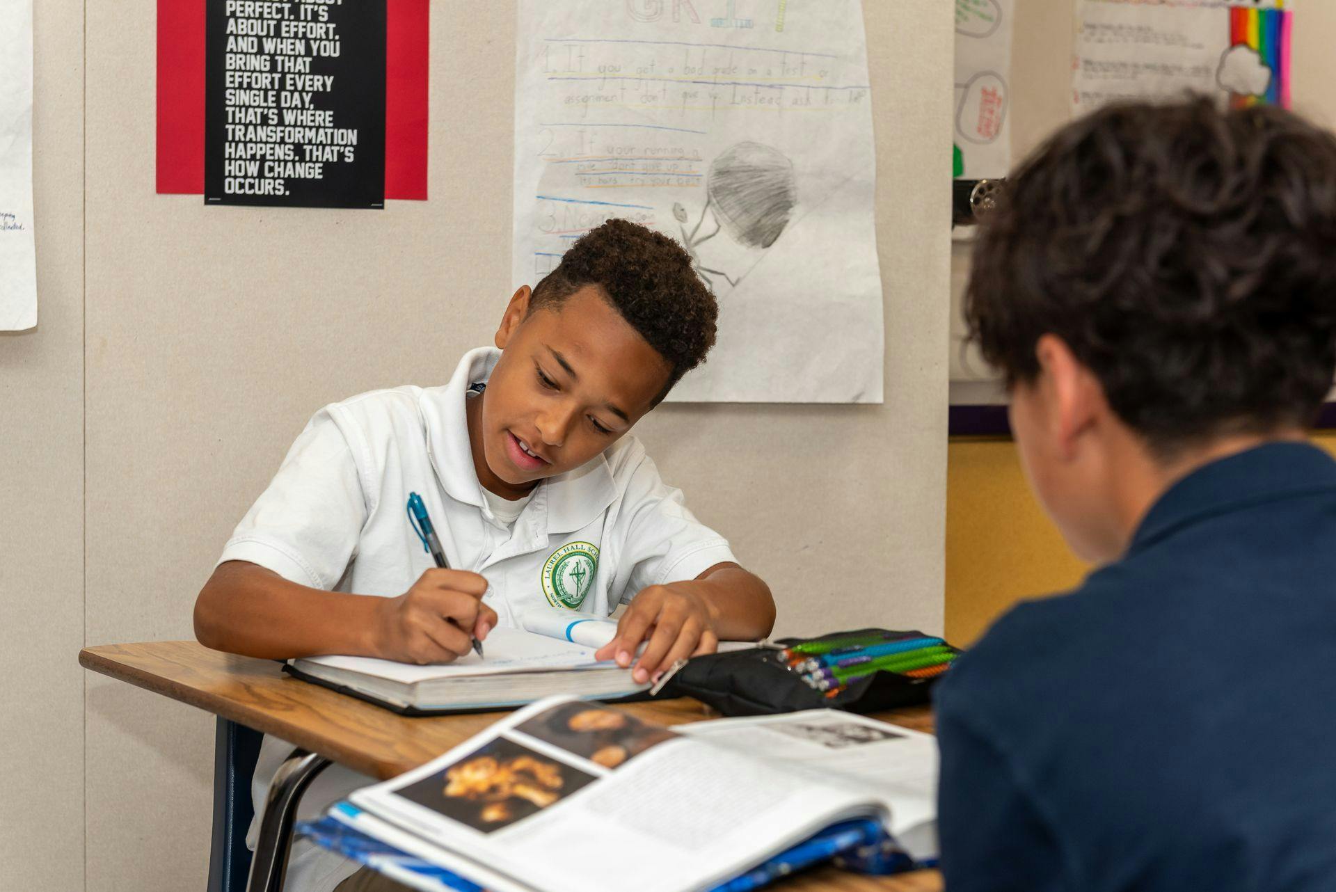 Child writing in a notebook at a desk in a classroom