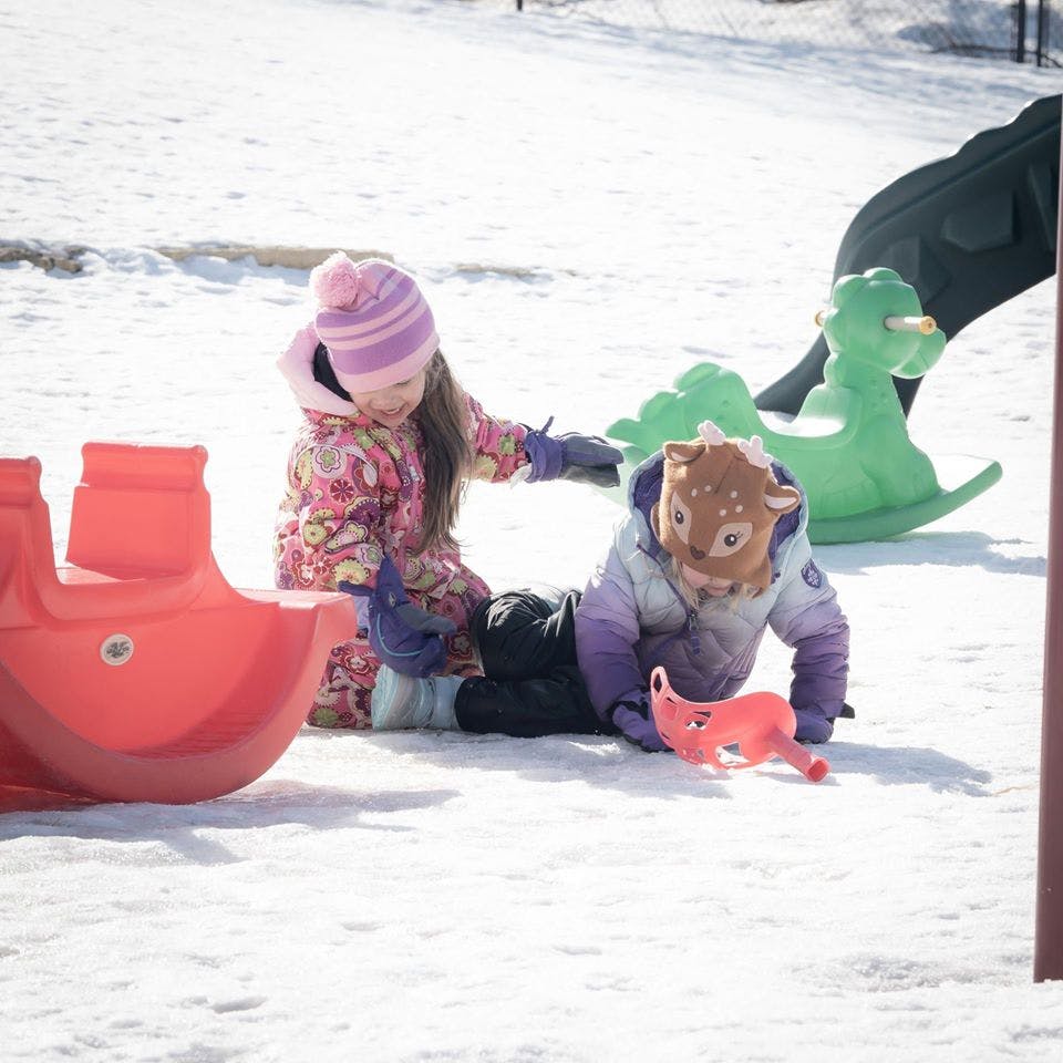 Two children playing in the snow with plastic toys