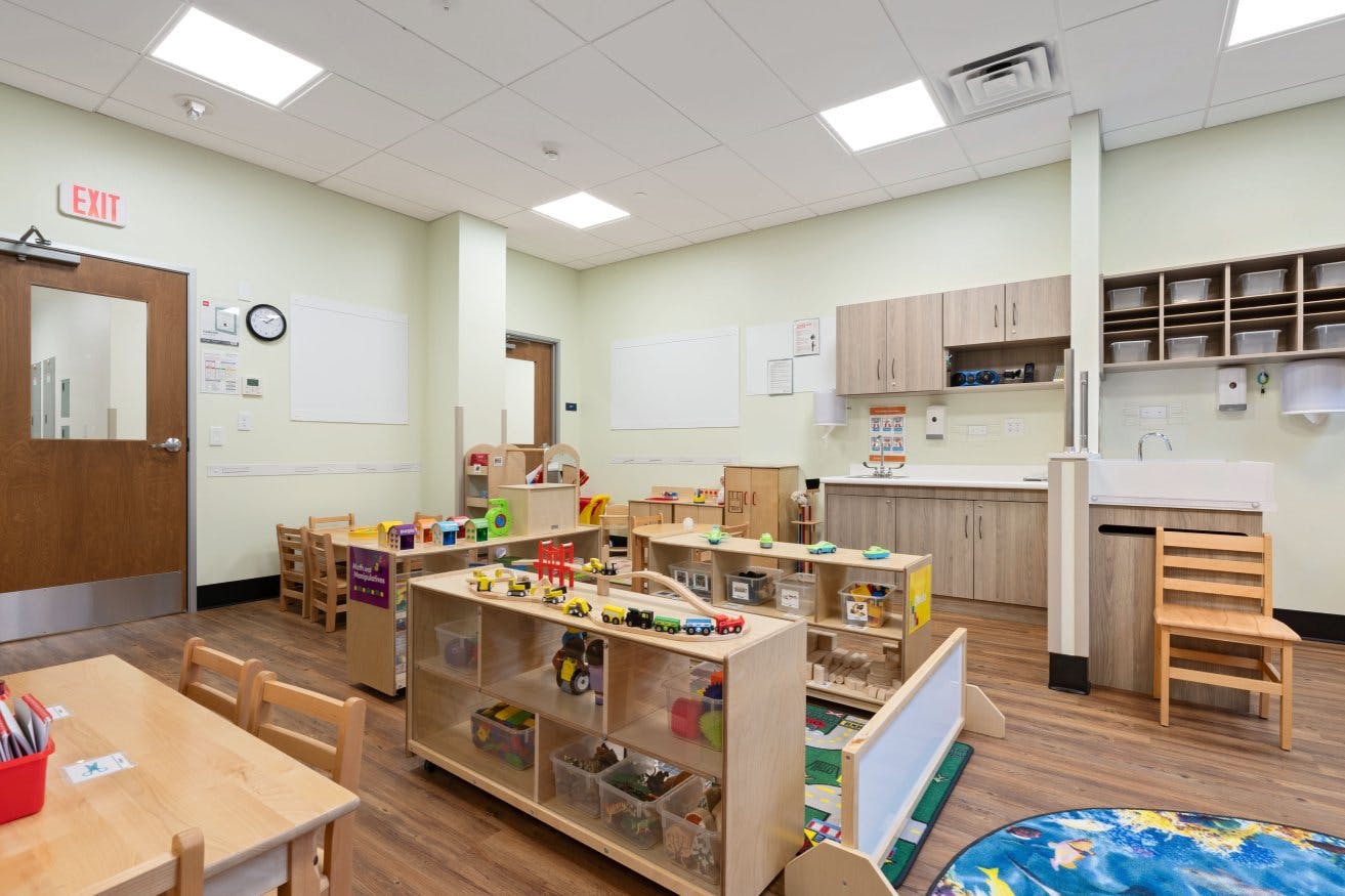 Empty classroom with small wooden tables, chairs, and shelves full of toys