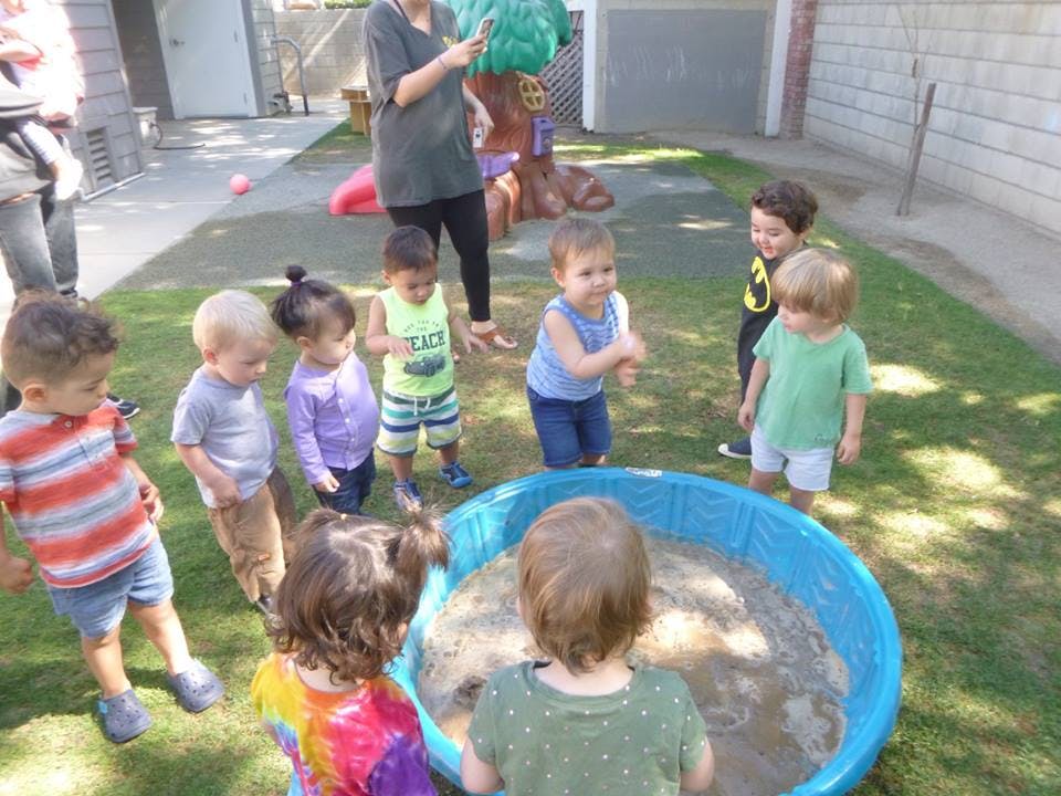 Children playing around a blue wading pool filled with mud