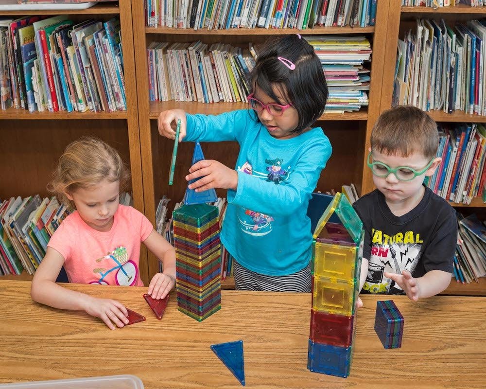 Three children playing with colorful magnetic building blocks
