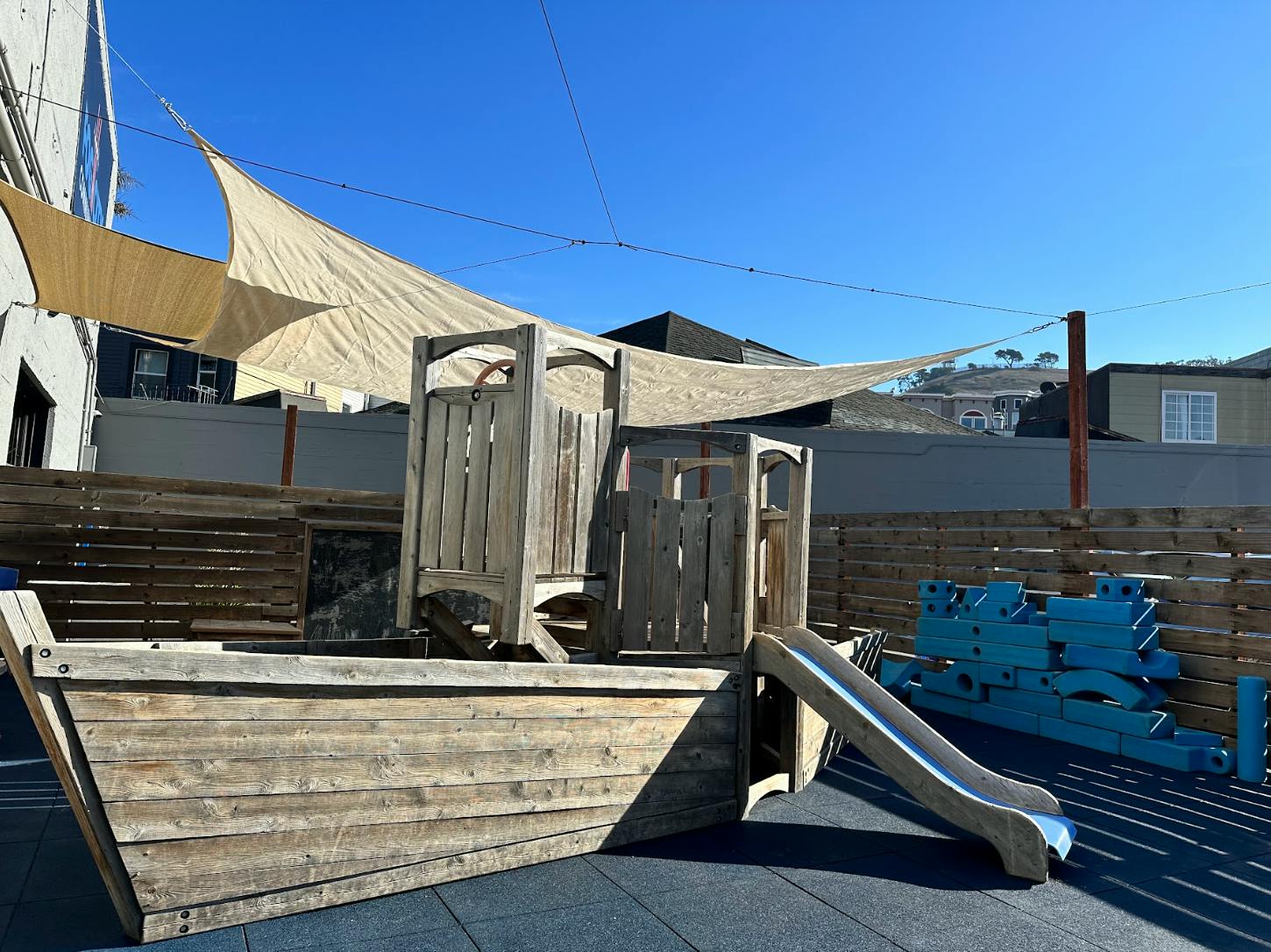 Wooden boat-shaped playground structure with a slide and shade sails