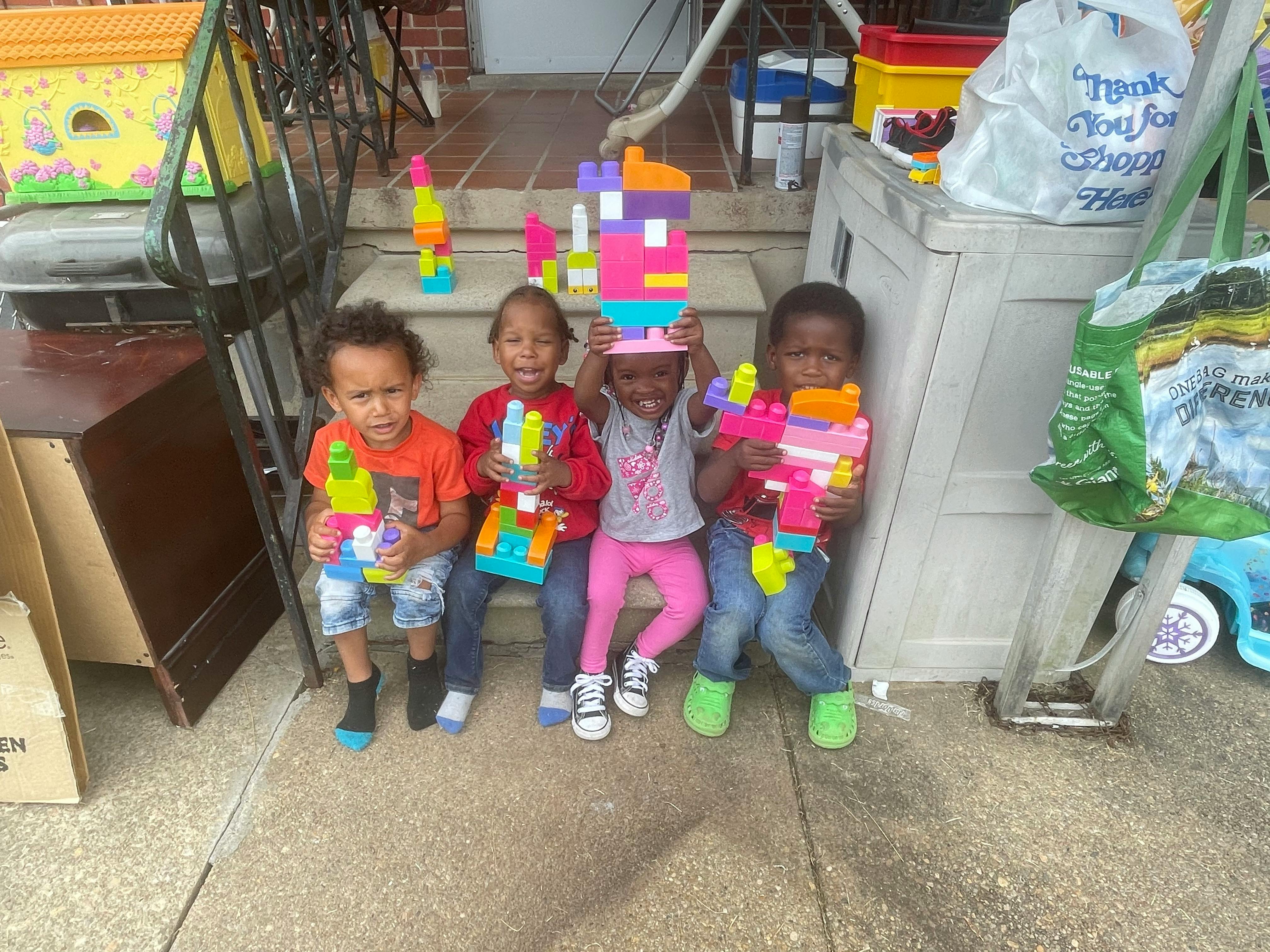 Four children sitting on steps holding colorful toy blocks and water guns