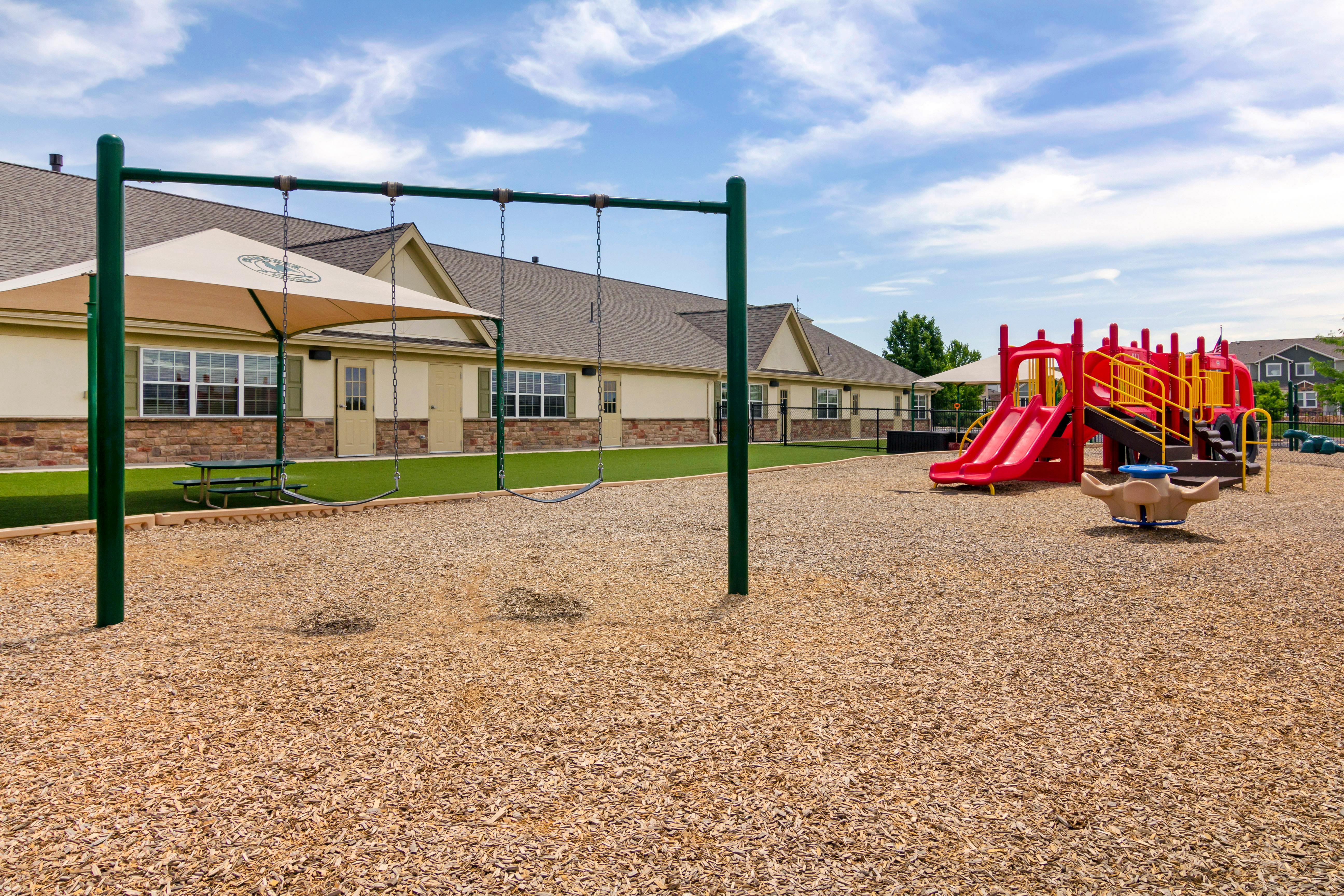 Swings and a red and yellow playground slide with a building in the background