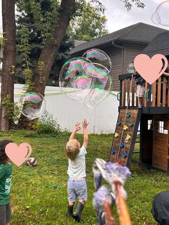 Child reaching up to large bubbles in a yard