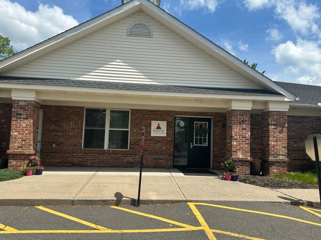 Brick building with white siding, a dark door, and a KinderCare sign