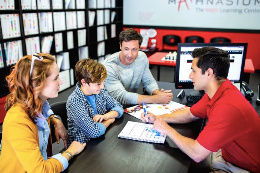 Four people gathered around a table with one person writing in a notebook